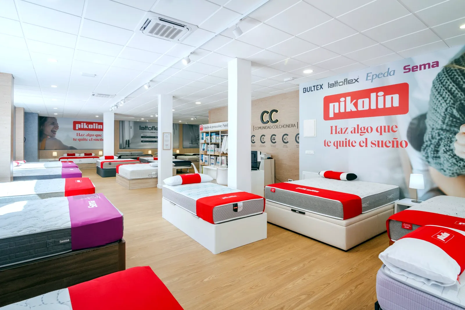 Exposición de colchones y canapés con el espacio Pikolin, el mural de marcas y el logotipo de Comunidad Colchonera en la tienda de Alcalá de Henares