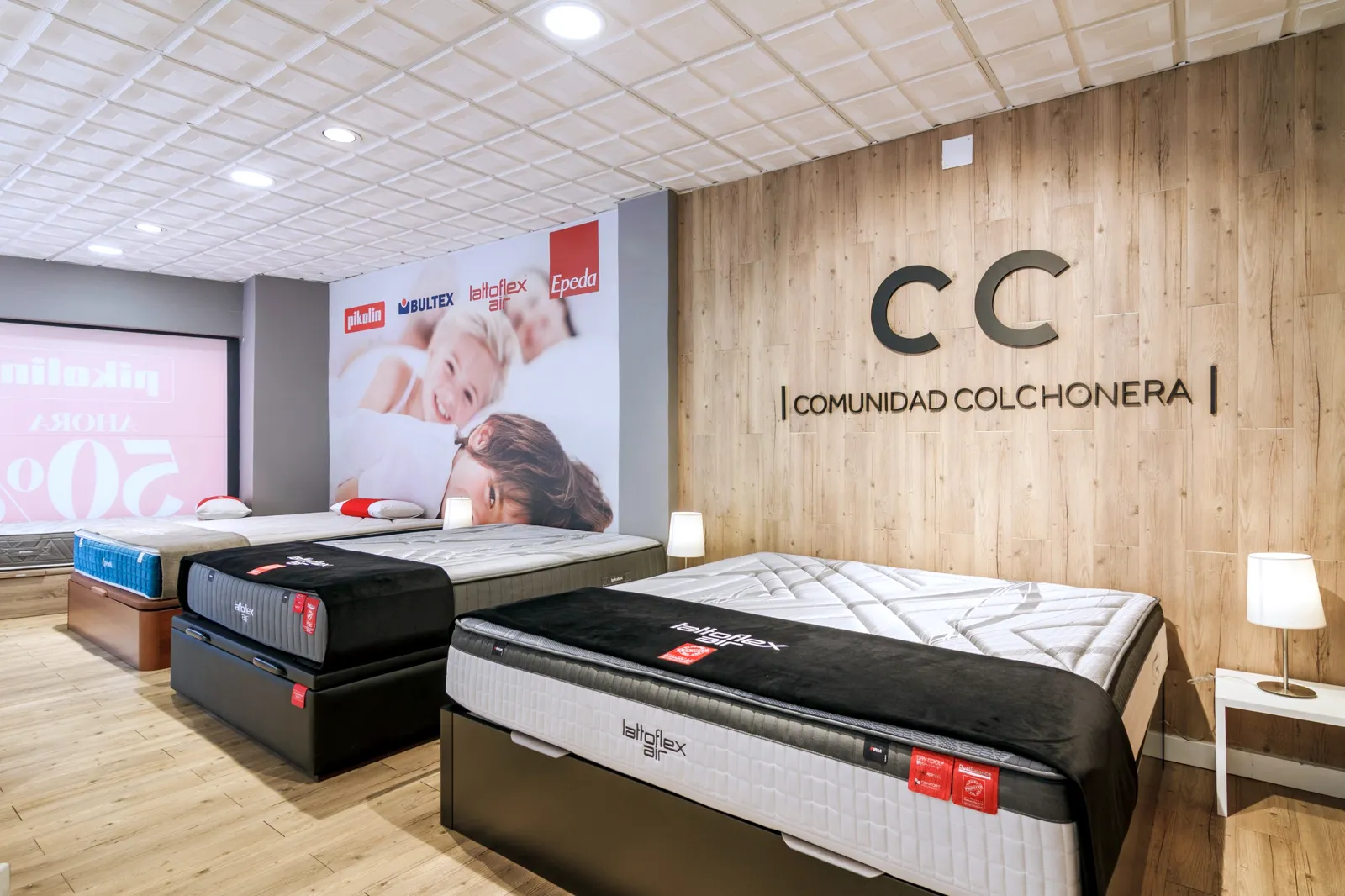 Colchones y canapés de Lattoflex frente a la pared de madera con el logotipo en la tienda Comunidad Colchonera de Getafe