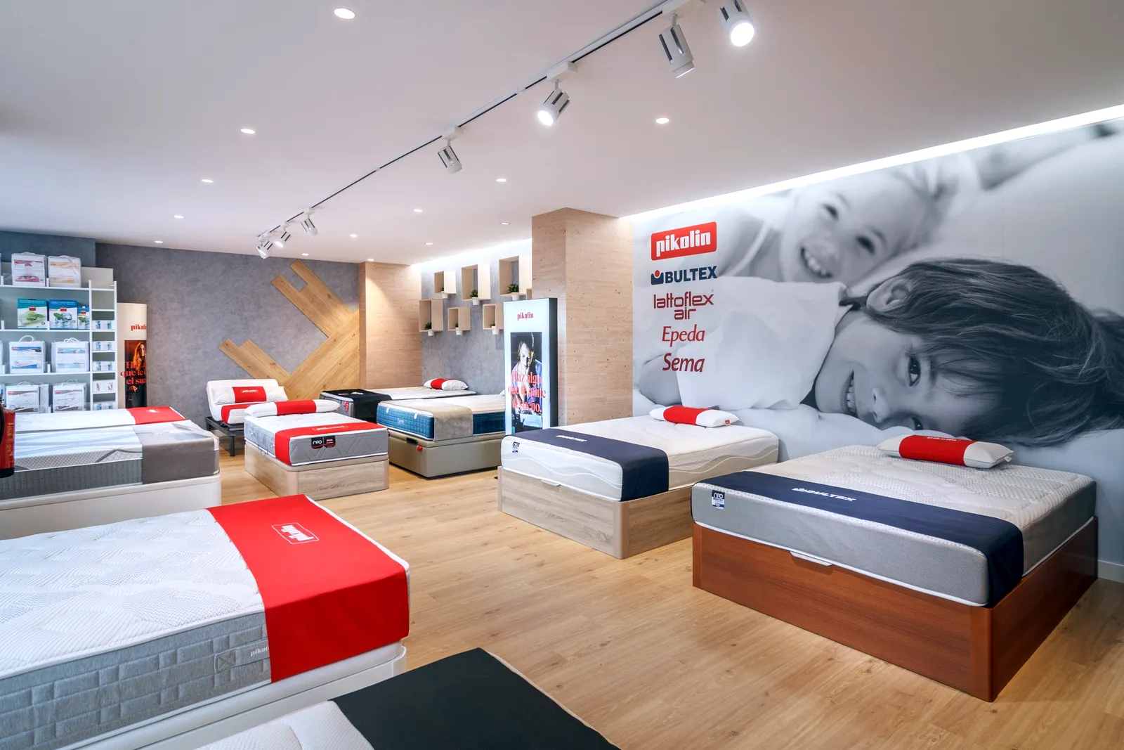 Exposición de colchones y canapés Pikolin y Bultex frente al mural con las marcas Pikolin, Bultex, Lattoflex, Epeda y Sema en la tienda Comunidad Colchonera de La Gavia, Madrid