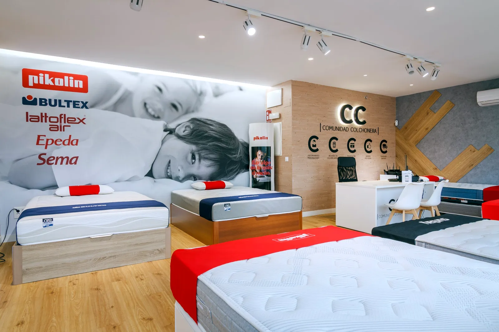 Colchones y canapés Bultex y Pikolin junto al mural de marcas y el logotipo de Comunidad Colchonera en la tienda de La Gavia, Madrid