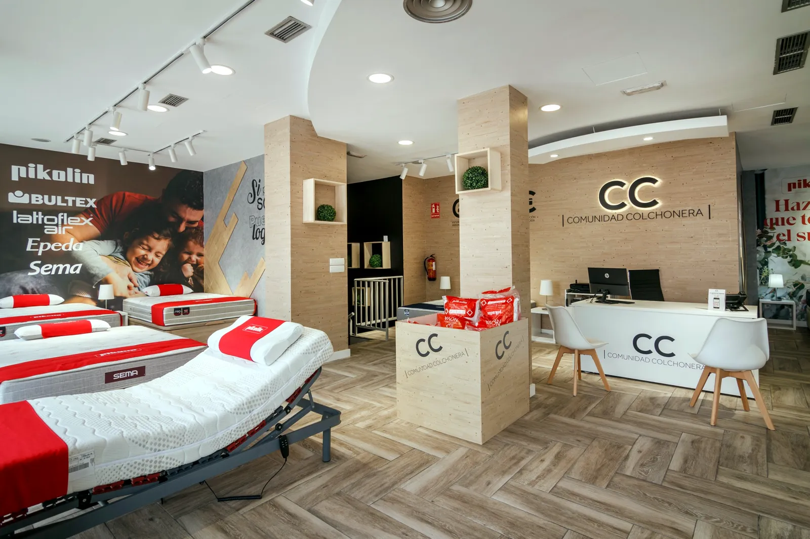 Interior de la tienda Comunidad Colchonera de Moratalaz, Madrid, con el mural de marcas Pikolin, Bultex, Lattoflex, Epeda y Sema, el mostrador y una cama articulada